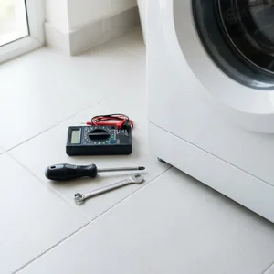 Screwdriver, spanner and multimeter laid out beside a washing machine.